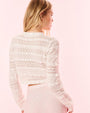 The backside view of a blonde model dressed in a white lace cardigan and white bottoms in front of a white background.