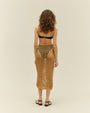 A full body backside view of a brunette model wearing a black bikini top with thin straps, and black bikini bottoms with a diamond rope-knit skirt over it. The model is also wearing black open-toed heels and is standing in front of a white background.