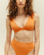 A close-up view of a brunette model wearing a bikini showcasing a high-waisted orange bottoms and a V-neck top. The background is plain white.
