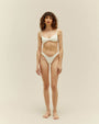 A full body frontal view of a barefoot brunette model wearing a white bikini with thin straps and a horizontal line in the middle of the top. The background is plain white.