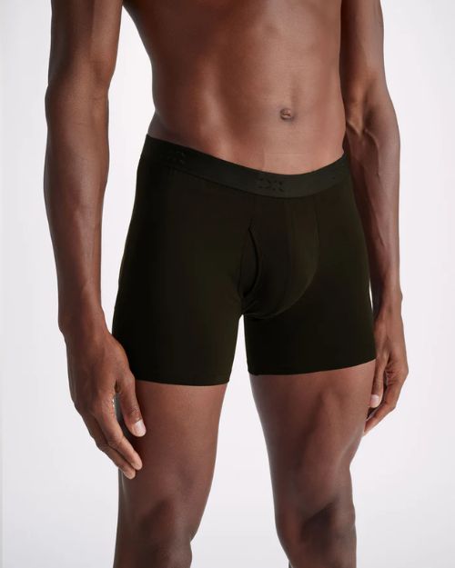 A close-up image of a model wearing a pair of black boxer briefs standing against a white background.