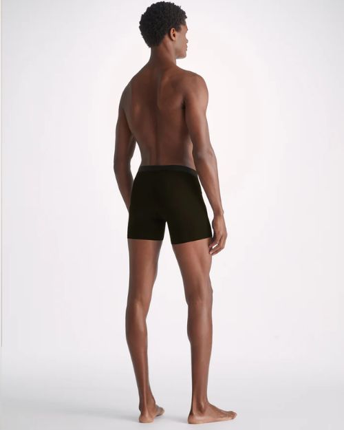 A full body backside view of a model wearing a pair of black boxer briefs standing against a white background.