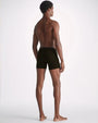 A full body backside view of a model wearing a pair of black boxer briefs standing against a white background.
