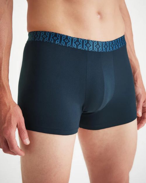 Up-close image of a shirtless model wearing a pair of navy-blue boxer briefs with nautical knots print along the waistband. The background is white.