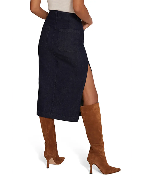 The backside view of a model's lower body wearing a white shirt tucked into a dark blue denim skirt with a high slit on the side, paired with brown suede knee-high boots.