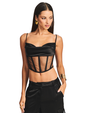 A knee-up view of a brunette model wearing a cropped, black, thin strapped sheer corset-style top with a fully black fabric chest area, paired with black cargo pants and square gold earrings. The background is plain white.