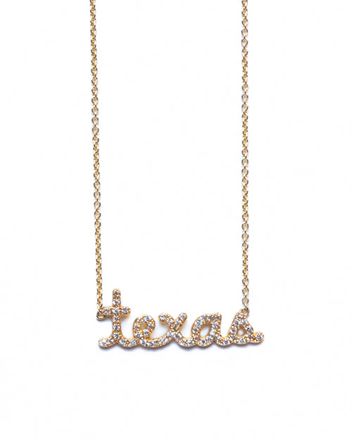 A pendant reading "TEXAS" in lowercase cursive letters, attached to a gold chain. The necklace is hanging over a white background.