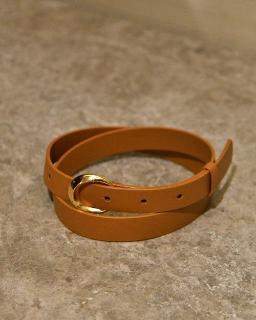 Camel-colored leather belt with gold buckle placed on marbled cement surface.