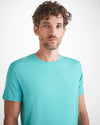 An image of a man from the waist up wearing a short sleeve plain turquoise shirt