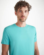 An image of a man from the waist up wearing a short sleeve plain turquoise shirt