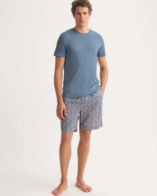 A man dressed in a blue t-shirt and shorts poses in a relaxed manner.
