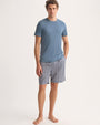 A man dressed in a blue t-shirt and shorts poses in a relaxed manner.
