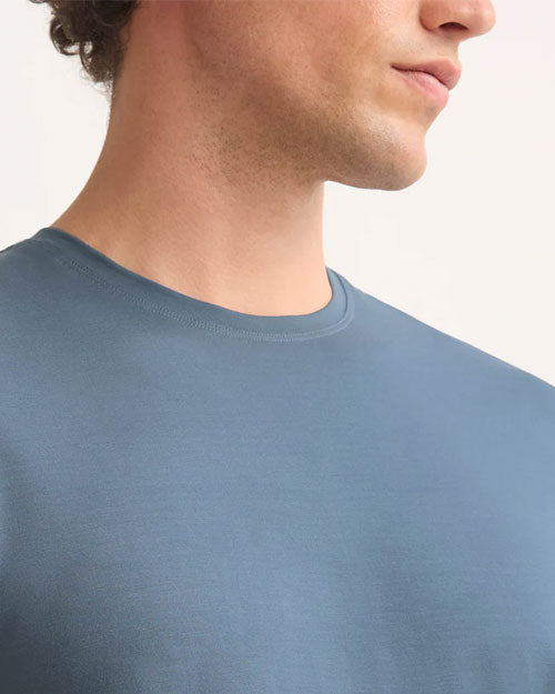  A man wearing a blue t-shirt stands confidently, showcasing a casual and relaxed style.