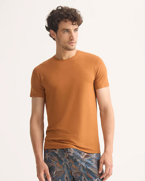 A man wearing an orange t-shirt and shorts stands casually