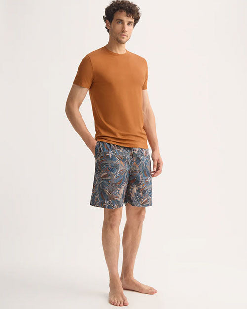 A man wearing an orange t-shirt and shorts stands casually.