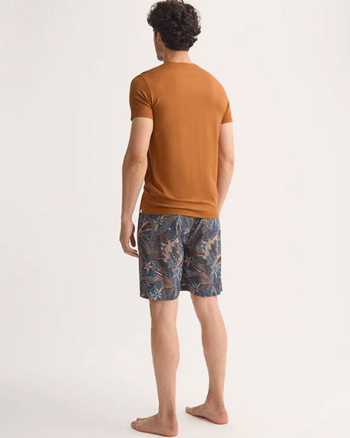 A man wearing an orange t-shirt and shorts stands backwards casually