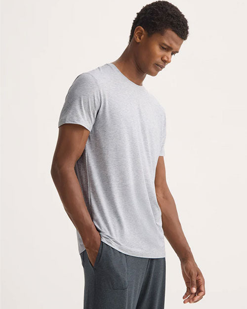 A man wearing a grey t-shirt and sweatpants stands casually, showcasing a relaxed outfit.