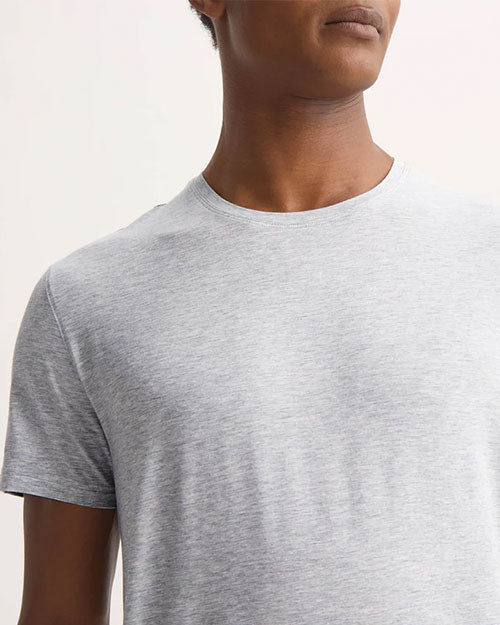 A man dressed in a grey t-shirt poses, highlighting a simple and comfortable outfit.
