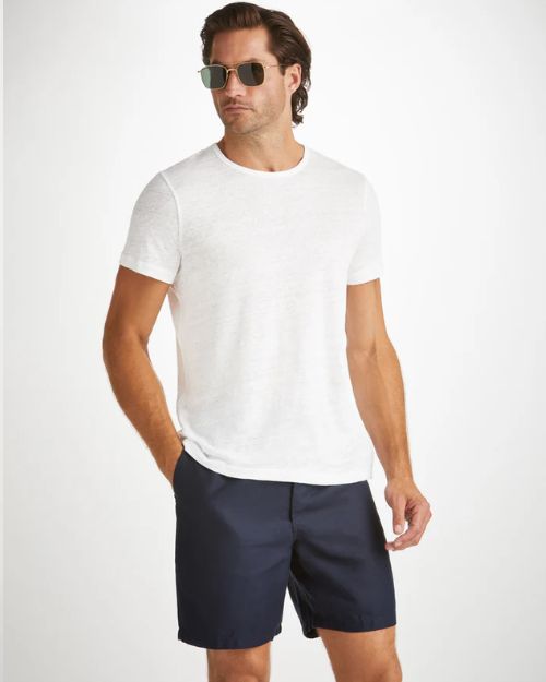 A man standing wearing sunglasses, a short-sleeve white t-shirt, and navy-blue shorts 