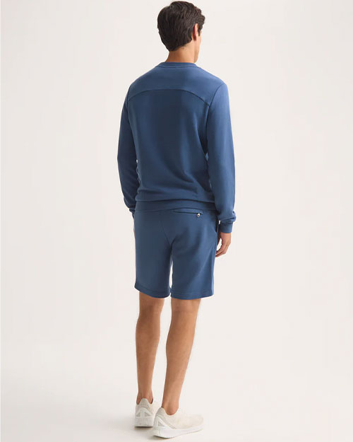 Back view of a man in a blue sweatshirt and shorts, casually standing.