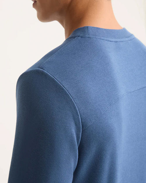 A man seen from behind, dressed in a blue sweatshirt, looking away from the camera.