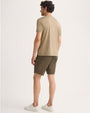 Man seen from behind, wearing a taupe-colored t-shirt and shorts, with a casual stance.