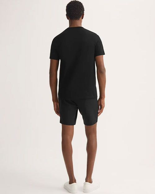 Man seen from behind, wearing a black t-shirt and shorts, with a casual stance.