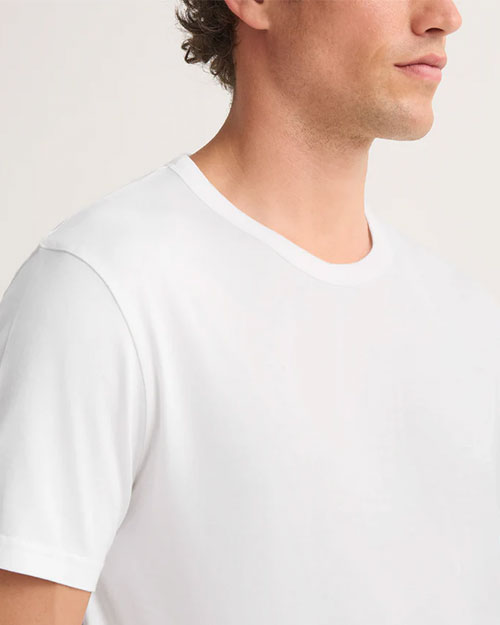 A man wearing a plain white t-shirt stands against a neutral background.