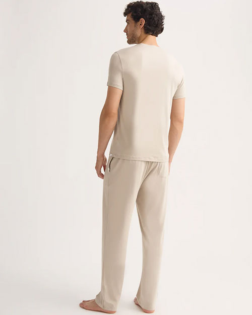 A man standing backwards in a beige t-shirt and pants stands, embodying a simple and relaxed fashion choice.