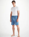 A man standing with a white t-shirt and blue jersey lounge shorts that have a drawstring waist with two pockets on the front of the shorts.  The shorts approach right above the knee.