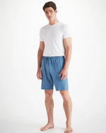 A man standing with a white t-shirt and blue jersey lounge shorts that have a drawstring waist with two pockets on the front of the shorts.  The shorts approach right above the knee.