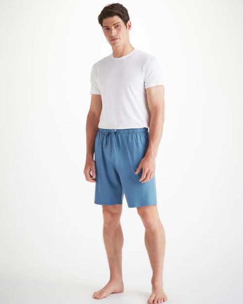 A man standing with a white t-shirt and blue jersey lounge shorts that have a drawstring waist with two pockets on the front of the shorts.  The shorts approach right above the knee.