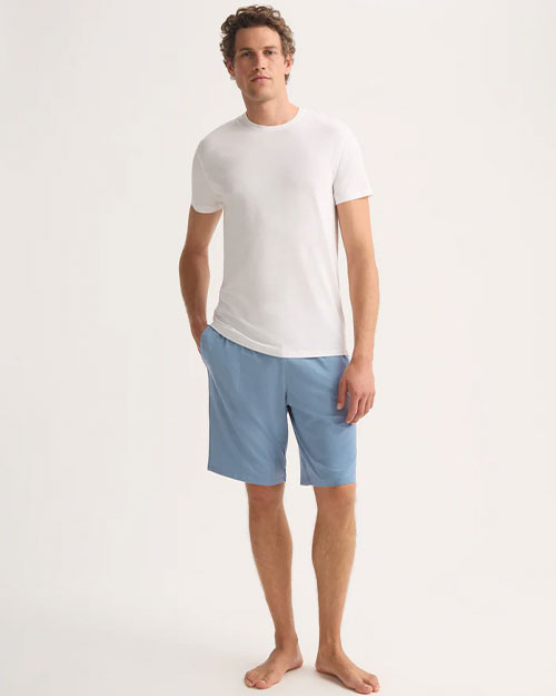A man dressed in a white t-shirt and blue shorts poses in a relaxed manner.