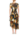 Back view of a person wearing a dark floral dress with short sleeves, a round neckline, and an asymmetrical ruffled hemline. The floral pattern features yellow, orange, and green tones. 