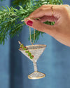 A hand holds a martini glass ornament adorned with green leaves, showcasing a festive and elegant decoration.