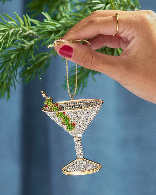A hand holds a martini glass ornament adorned with green leaves, showcasing a festive and elegant decoration.