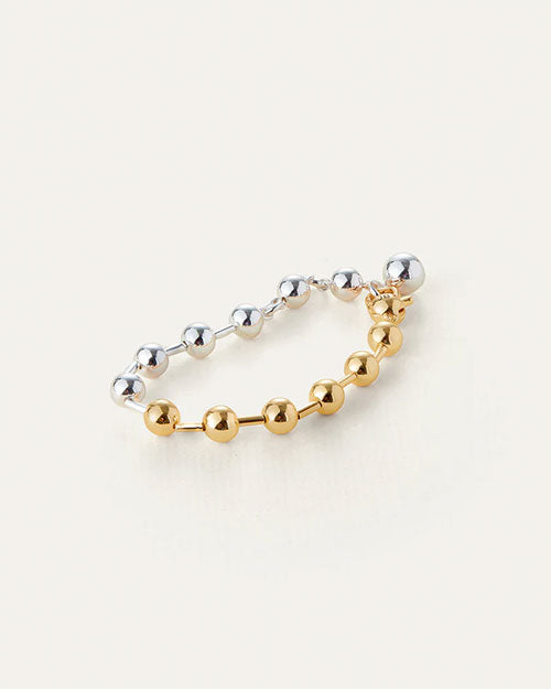 A two-toned, half silver and gold bracelet with round beads evenly spaced around it, and a dangling sphere charm.