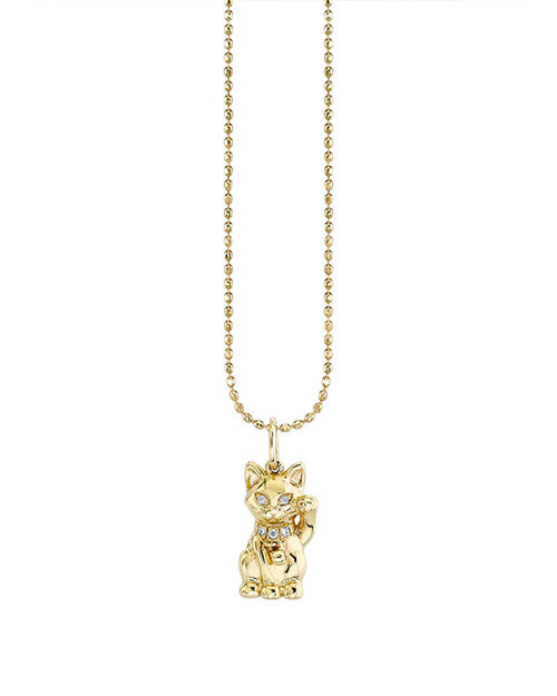 Gold necklace with a cat-shaped pendant featuring gemstone eyes and a jeweled collar, hanging from a beaded gold chain.