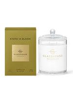 A product from Glasshouse Fragrances named ‘Kyoto in Bloom.’ The image shows a gold-colored packaging box on the left and a candle in a glass container with a lid on the right. The box indicates that it is a soy candle , weighing 380g or 13.4 oz.