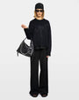 Woman with a black sweater, black pants, and a black handbag on a white background. 