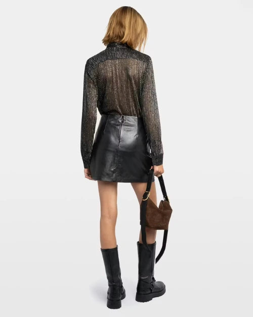 Backside of a person wearing a metallic black top, black mini skirt, black boots, and a brown handbag on a grey background. 