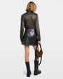 Backside of a person wearing a metallic black top, black mini skirt, black boots, and a brown handbag on a grey background. 