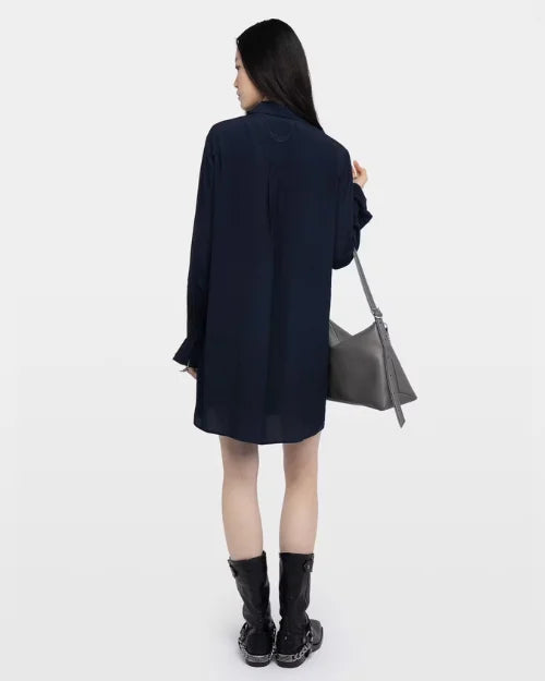 Backside of a woman in a navy dress, black boots, and a silver handbag on a white background. 