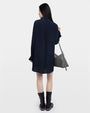 Backside of a woman in a navy dress, black boots, and a silver handbag on a white background. 