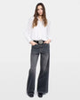 Photo of a woman with a white long sleeved blouse, grey denim jeans, and a silver belt against a white background.