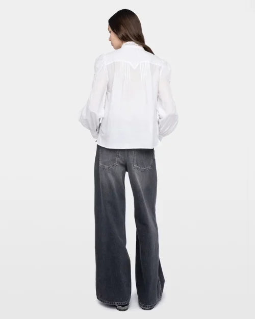 Backside photo of a woman wearing a white long sleeve top and grey jeans against a white background. 