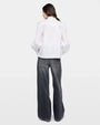 Backside photo of a woman wearing a white long sleeve top and grey jeans against a white background. 