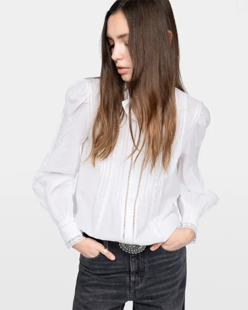 Picture of a woman wearing a white, long-sleeved blouse and grey jeans against a white background. 