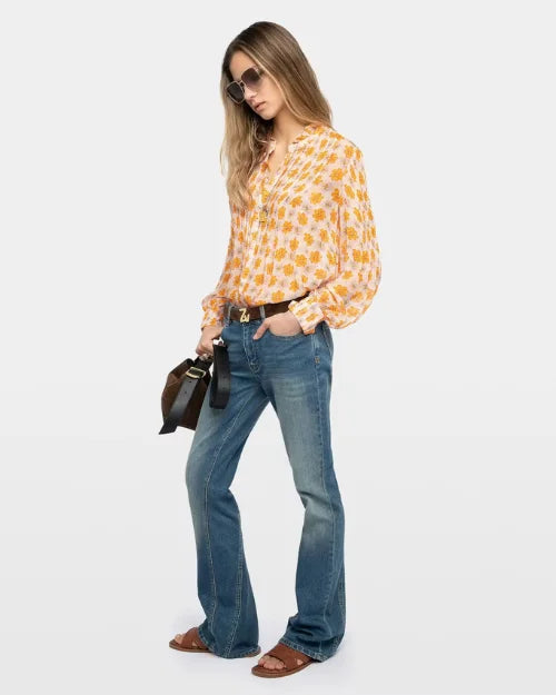 Image of a woman wearing sunglasses, an orange floral blouse, blue jeans, brown sandals and a brown handbag against a white background. 