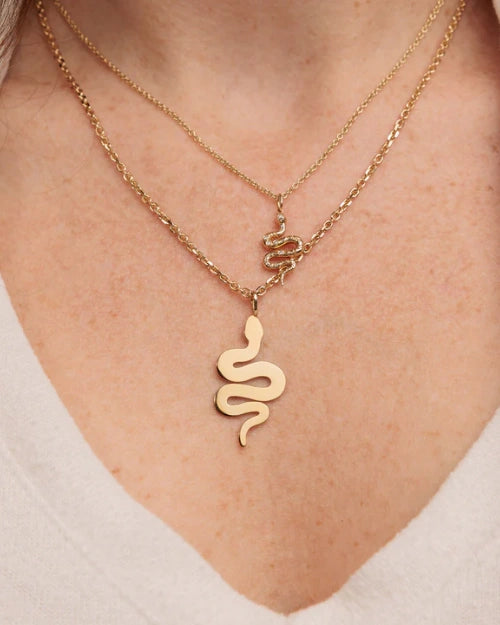 Close-up image of a model's neck wearing two gold snake pendant necklaces. 